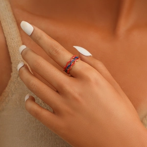 Macro detail of wave patterned gold ring with red and blue enamel inlay on finger