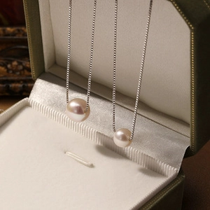 Close-up of two freshwater pearl necklaces with silver chains in an olive green gift box