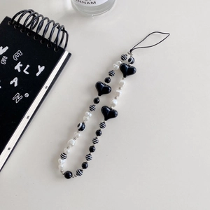 Detail shot of black heart beads and striped pearls phone charm on minimalist background