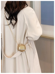 Detail of a mini gold metal wave-textured chain bag worn over a beige trench coat