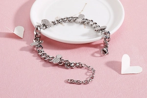 Detailed shot of silver pineapple charm bracelet on white ceramic plate with pink background