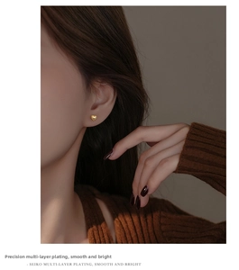 Close-up of gold heart stud earring worn by model showing multi-layer plating finish