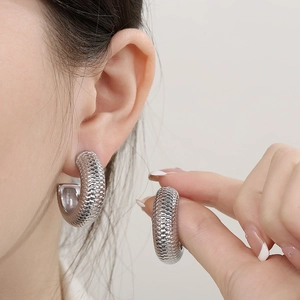 Gros plan de boucles d'oreilles C argentées avec texture d'écailles sur mannequin