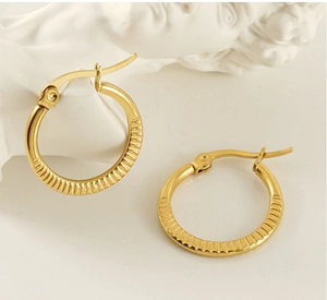 Macro detail of gold-plated hoop earrings with vertical ribbed textures and latch closure