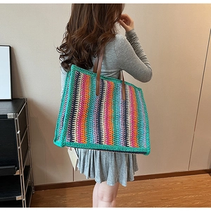 Detailed back view of a large colorful striped straw tote bag on a model's shoulder