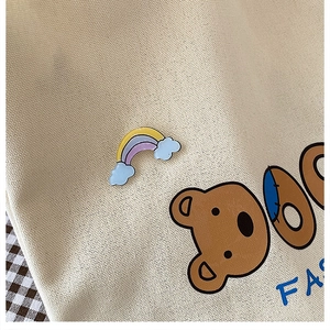 Regenbogen-Emaille-Brosche an beigefarbener Segeltuchtasche mit feiner Textur