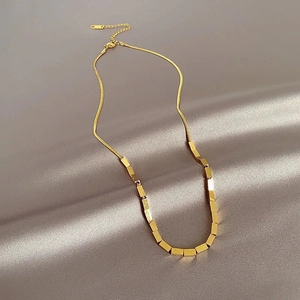 Minimalist titanium steel snake chain necklace with gold bars on beige silk background