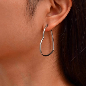 Close-up of a model wearing a large hollow heart-shaped silver earring with metal finish
