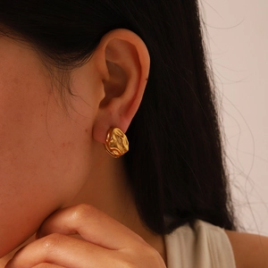 Gros plan d'un mannequin portant une boucle d'oreille dorée en acier à texture irrégulière