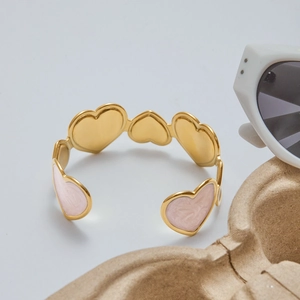 Detail view of heart-shaped gold bangle with pink marble enamel inlay on textured tray