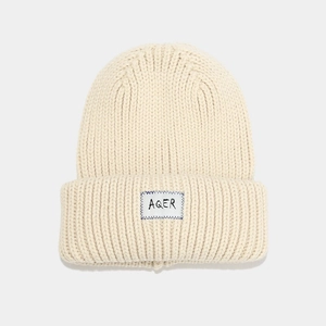 Close-up of thick beige knit beanie featuring AQER woven label and blue stitch detail