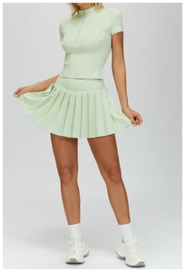 Detail of mint green pleated tennis skirt and slim fit zip-up top for athletic performance