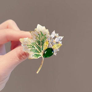 Golden maple leaf brooch featuring green zircons and sparkling crystals in hand
