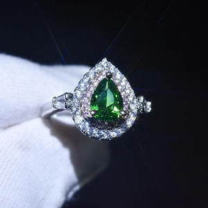 Macro shot of a green pear-shaped moissanite ring with a halo of diamonds on a silver band