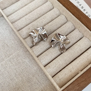 Detail showing irregular pleated silver flower earrings on a beige velvet jewelry tray