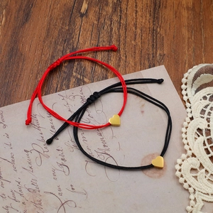Adjustable woven cord bracelets with gold heart pendants on vintage paper background