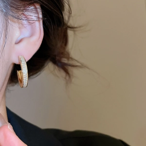 Close-up of elegant C-shaped gold earrings with zircon crystals worn by a model