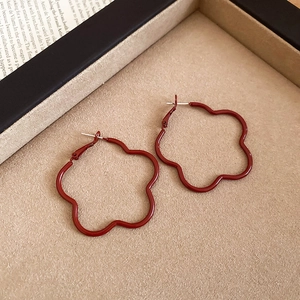 Close-up of deep red petal flower hoop earrings on a beige velvet jewelry tray