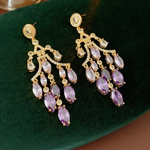 Detailed shot of gold drop earrings with purple marquise gems on green velvet