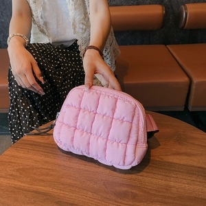 Detailed view of a pink quilted nylon crossbody bag held by a model in a cafe setting