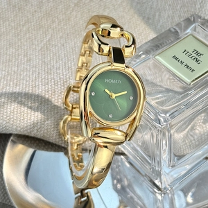 Detail of a green dial watch with a horseshoe case and golden bangle strap on a linen background