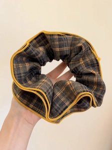 Detailed view of gray and orange checkered hair scrunchie with bright yellow edge stitching