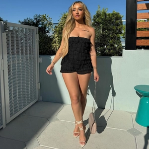 Detail of black strapless romper featuring layered ruffles and slim fit design