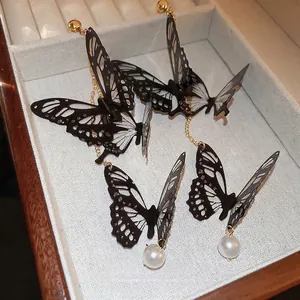 Boucles d'oreilles papillon avec design noir ajouré et perles blanches dans un écrin
