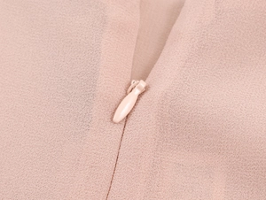 Dettaglio della cerniera invisibile su un abito in pizzo rosa cipria con texture in chiffon