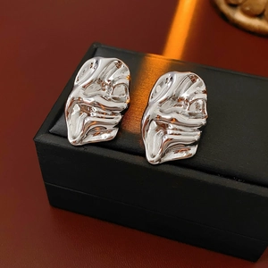 Close-up of silver earrings with irregular pleated metal texture on a black jewelry box