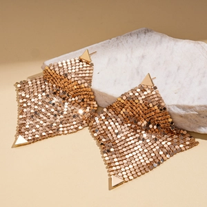 Macro detail of golden geometric mesh earrings on a white stone background for a trendy look