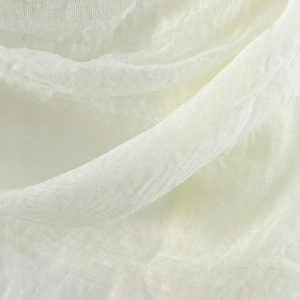 Close-up of white crinkle cotton scarf fabric showing soft pleated texture and fringe