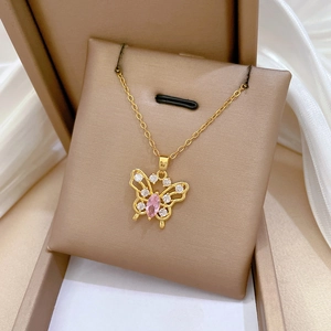 Macro shot of gold butterfly pendant with pink oval stone and crystals on silk fabric