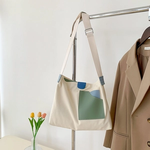 Detail of beige canvas tote bag with green PU pocket and blue trim on metal hanger
