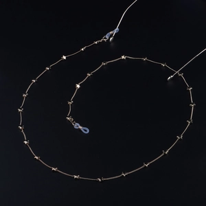 Detailed flat lay of golden eyewear chain featuring delicate star charms on a dark backdrop