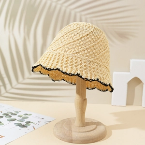 Chapeau cloche en paille beige avec bord ondulé noir sur support bois pour les vacances