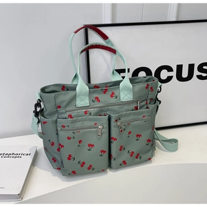 Detail of green canvas tote with red cherry print featuring multiple utility front pockets