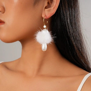 Close-up of elegant C-shaped gold earring with white faux fur pompom and pearl drop