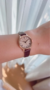 Detail of rose gold watch with beige dial and brown leather strap on female wrist