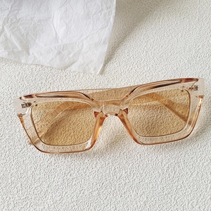 Close-up of translucent brown rectangular sunglasses with silver metal hinges on textured surface