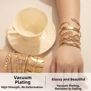 Detail of stacked gold stainless steel bracelets with leaf and braided textures