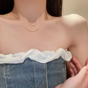 Close-up of a double-layered gold necklace featuring a white pearl and curved bar charm