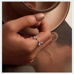 Macro shot of silver bird open ring with detailed wings held against a warm background