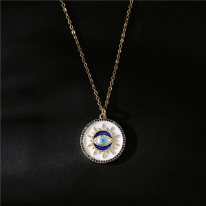 Gold evil eye necklace with white enamel pendant and blue zircon inlay on black background