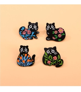 Macro shot of four black cat enamel pins featuring colorful floral patterns and zinc alloy finish