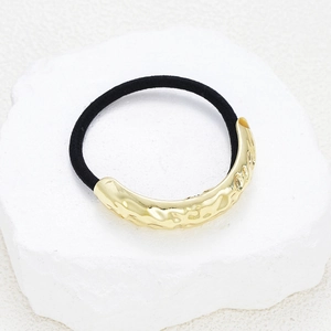 Detail of a black elastic hair tie featuring a textured gold metal buckle on a white stone