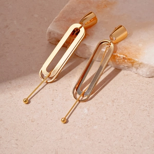 Detail of gold double-layer geometric earrings with oval links on a textured stone surface