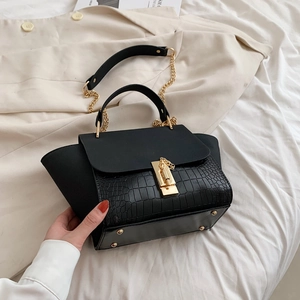 Detail of black crossbody bag with faux crocodile texture and gold metal clasp