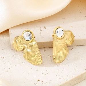 Detail of gold square earrings with transparent stones on a textured stone base