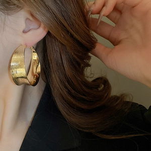 Close-up of model wearing wide gold C-shaped metal earrings with a brushed texture finish